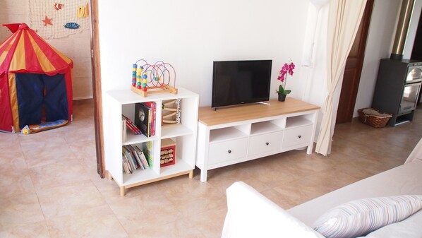 A living room with a white entertainment unit, a television, a small plant, and a colorful tent in the corner.