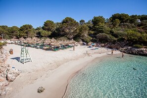 A beach with clear turquoise water, a sandy shore, and thatched umbrellas.