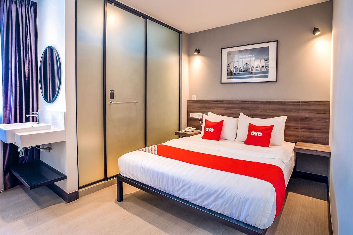 Une chambre d’hôtel moderne comprenant un lit, une table de chevet, une commode, un miroir, une porte coulissante et un tableau encadré au mur.