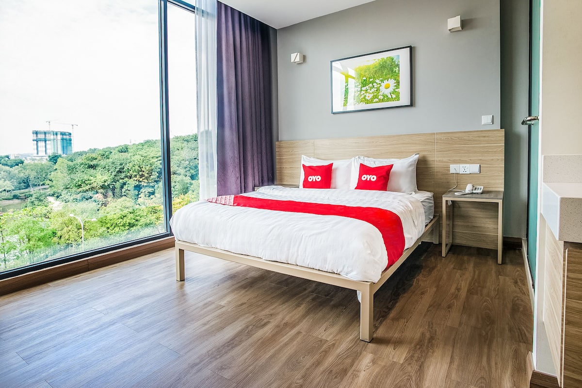Une chambre d’hôtel moderne avec un grand lit, une table de chevet, une vue sur la verdure et un tableau encadré au mur.