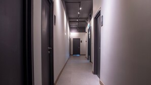 Un pasillo largo y estrecho con puertas oscuras a ambos lados, que conduce a una puerta al final.