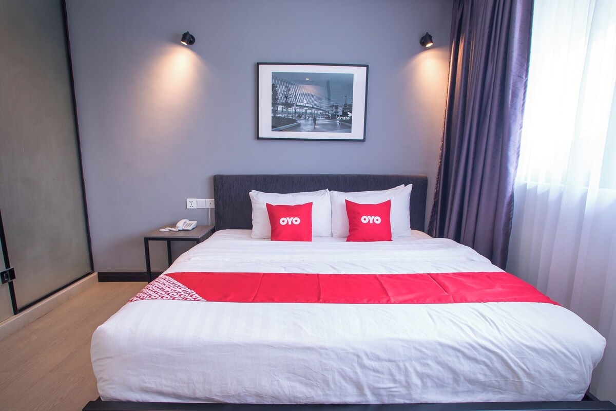 Une chambre d’hôtel avec un lit, deux oreillers rouges ornés du mot « OYO », un tableau encadré au mur et une table de chevet avec un téléphone.