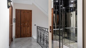 Un pasillo con puerta de madera, barandilla de metal negro y ascensor de vidrio.