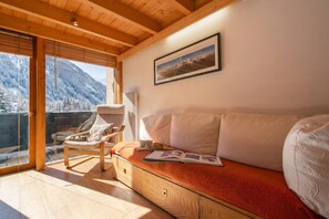 A cozy room with a wooden ceiling, a sofa with a red cushion, a chair, and a large window overlooking a snowy mountain. - Grand Roc C213 280m from Slopes, Mont-Blanc View, Parking & WiFi, Argentière (Chamonix), France (Argentière (Chamonix))