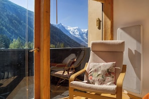 Un balcón con vistas a montañas nevadas, una silla de madera con cojín y un ventanal de vidrio.