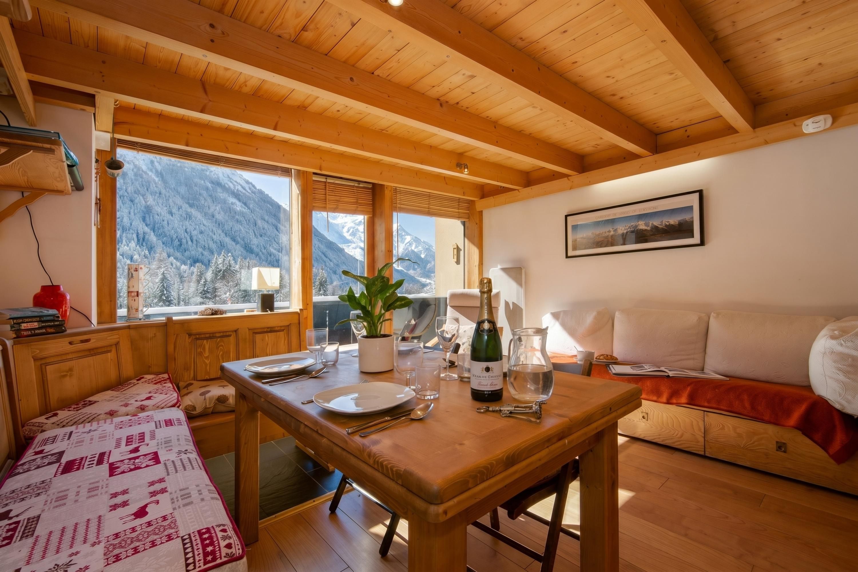 A cozy room with a wooden table set for dining, a sofa, and a view of snow-covered mountains through large windows.
