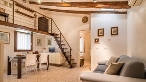 A spacious living area with a staircase, a sofa, a dining table with chairs, and artwork on the walls.