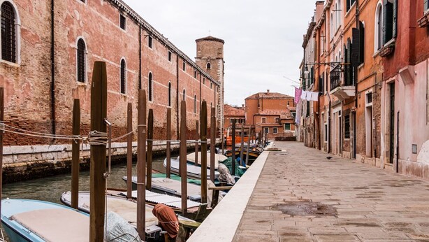 A narrow canal with boats docked along the sides, flanked by historic buildings with arched windows and a brick facade.