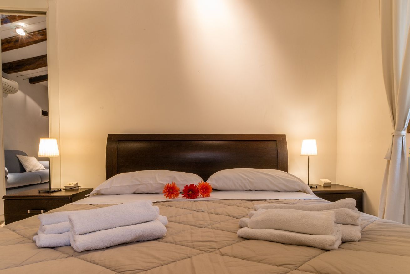 A neatly made bed with white linens and a quilted cover, two bedside lamps, and a nightstand with a lamp.
