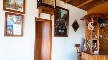 A room with wooden beams, a wooden door, and a shelf with various items including a radio, framed pictures, and a chair.