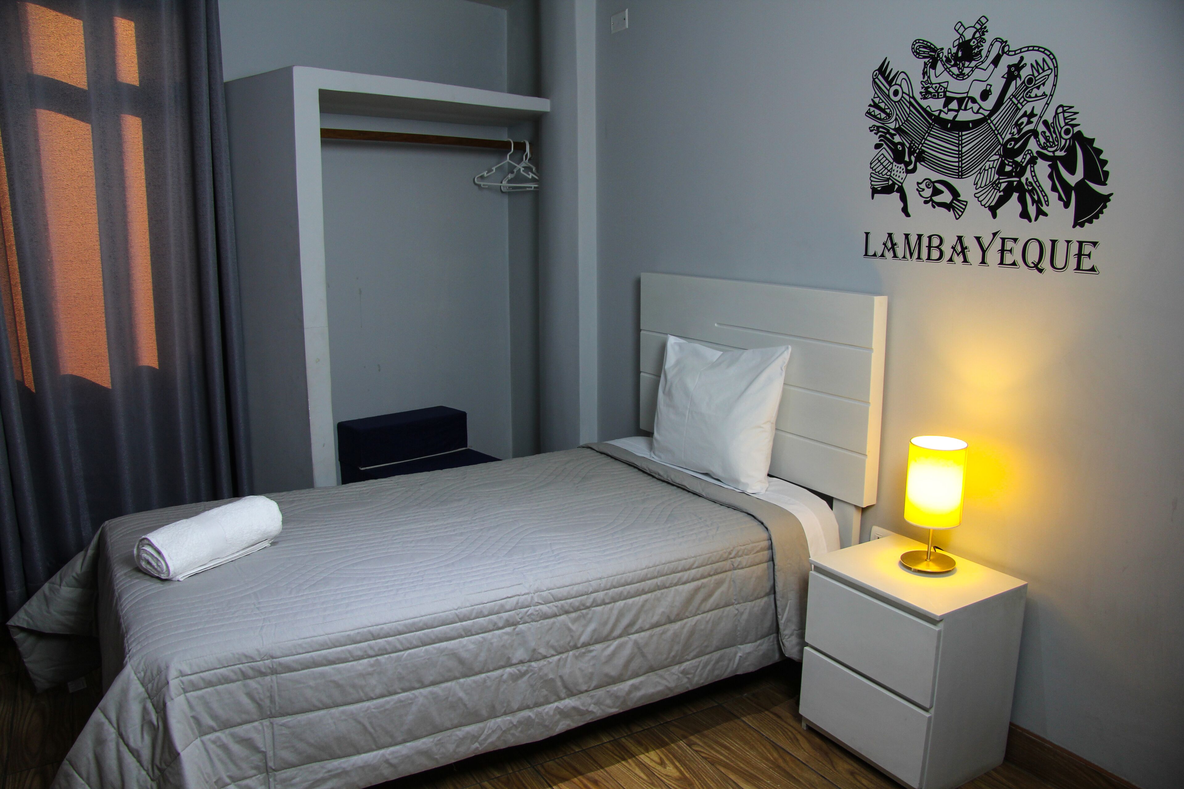 Habitación de hotel con cama, mesita de noche con lámpara, armario y un adhesivo en la pared.