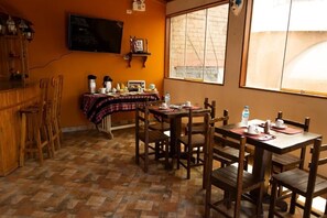 A dining area with wooden furniture, a television mounted on the wall, and a large window with a view of the outside.
