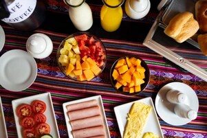 Una mesa de desayuno con diversos alimentos, como rodajas de tomate, jamón, huevos revueltos y fruta.