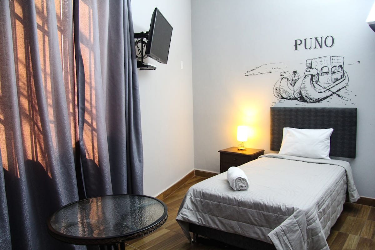 Une chambre d’hôtel avec un lit, une petite table, un téléviseur fixé au mur et une œuvre d’art décorative.