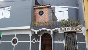 Un edificio con una torre de ladrillo, un portón negro y un balcón con plantas.