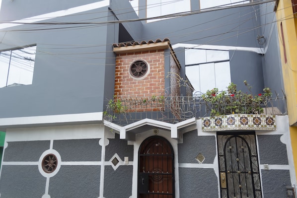 A building with a brick tower, a black gate, and a balcony with plants.