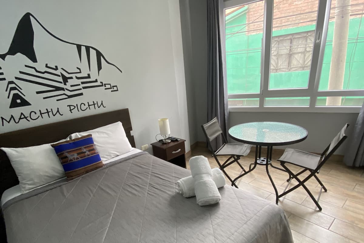 Une chambre d’hôtel avec un lit, une petite table et une fenêtre avec des rideaux.