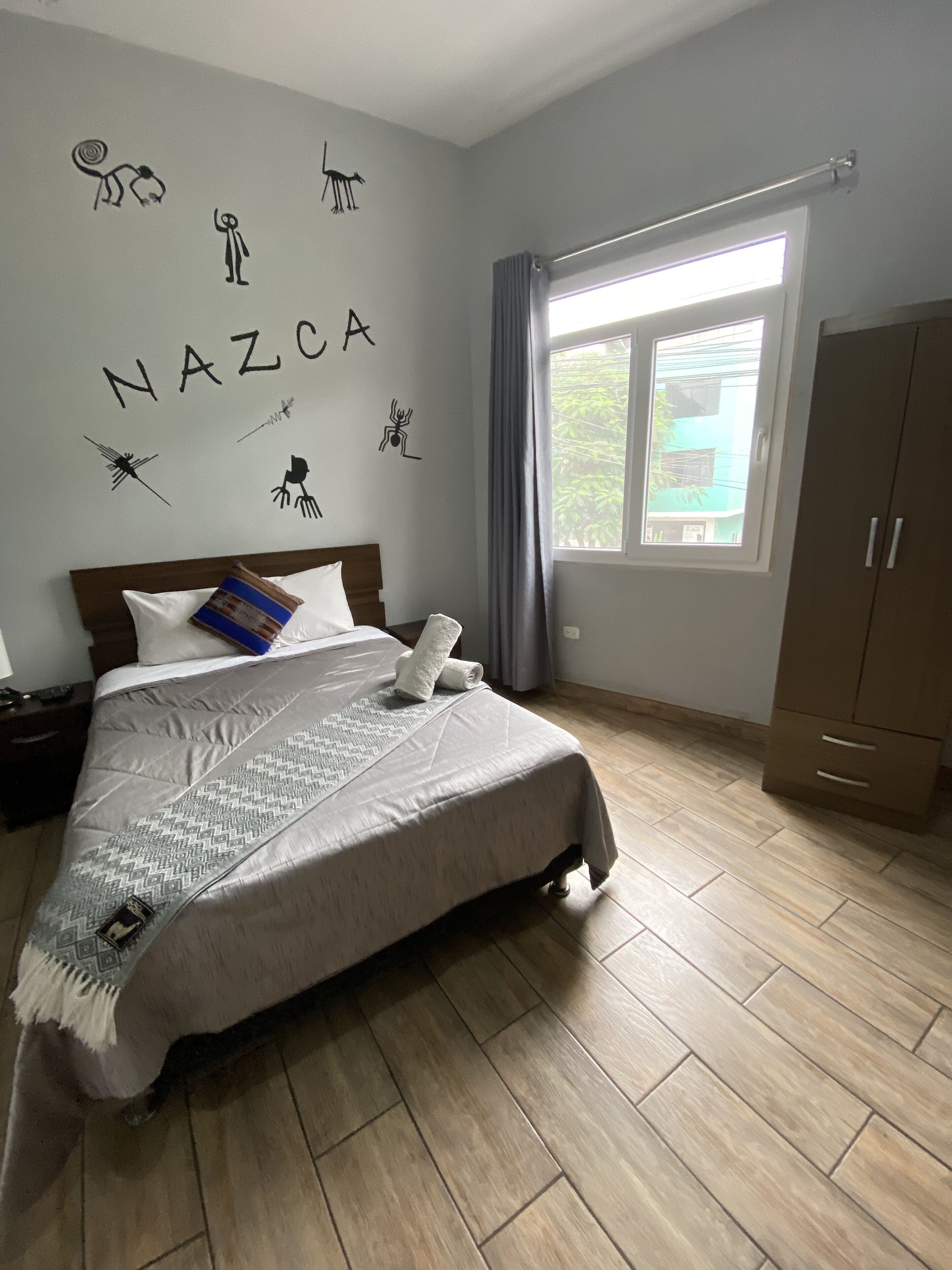 Ett sovrum med en säng, en garderob, ett fönster med gardiner och väggdekorationer, inklusive ordet ”NAZCA”.