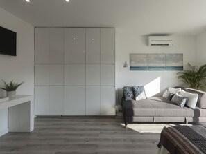 Ein modernes Wohnzimmer mit grauem Sofa, einem Flachbildfernseher und einem großen Fenster.
