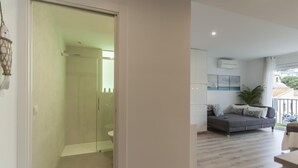 A modern apartment with a glass-enclosed shower, a grey sofa with patterned cushions, and a view of the outside. - AMAZING STUDIO in the CENTER of TOSSA (Tossa de Mar)