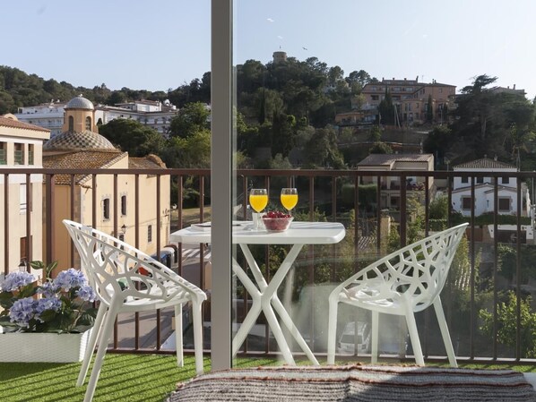 Ein Balkon mit weißen Stühlen und einem Tisch, ein Glas Orangensaft und eine Schale Erdbeeren.