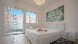 A modern bedroom with a large bed, a view through a glass door, a tiger painting on the wall, and a small nightstand. - Prestige du Lac 27 with Balcony and Parking, Lugano, Switzerland (Lugano)