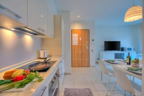 A modern kitchen with a stove, microwave, and a dining area with a table and chairs. - Prestige du Lac 27, Lugano, Switzerland (Lugano)