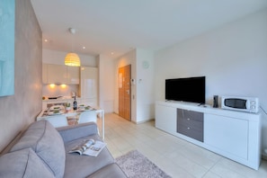 A modern living room with a sofa, a dining table, a kitchen area, and a TV.