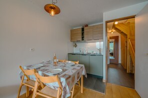 Een eetgedeelte met een tafel voor vier personen, houten stoelen en een hangende lamp.