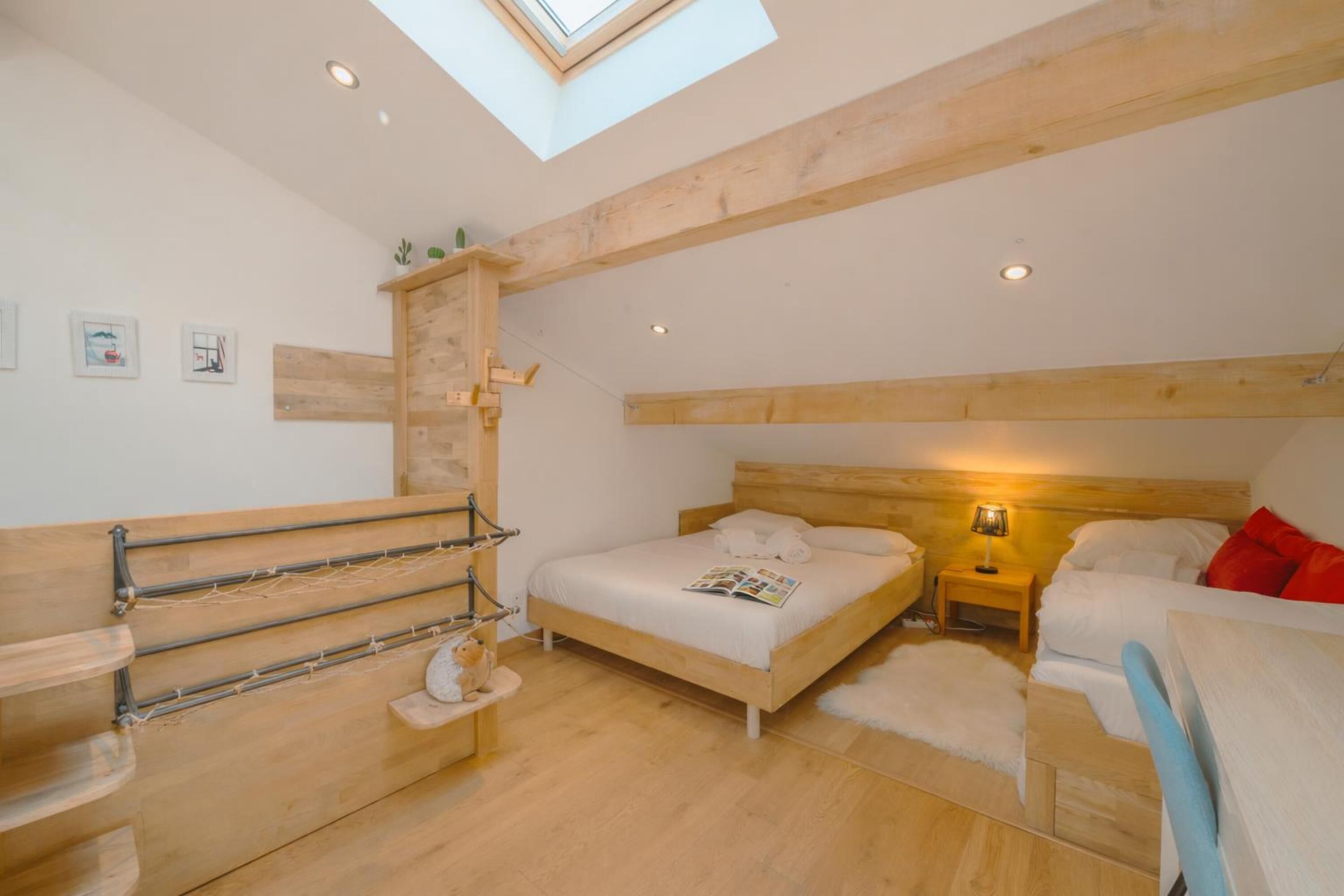 A bedroom with a skylight, wooden beams, a bed with white bedding, a nightstand with a lamp, and a small shelf with decorative items.