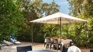 An outdoor dining area with a covered table and chairs, surrounded by trees and gravel. - BEAUTIFUL HOUSE IN TOSSA (Tossa de Mar)
