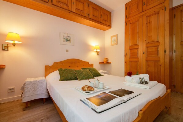 A neatly made bed with pillows, a bedside table with a lamp, and a tray with a croissant and coffee cups. - Bel'Alp 16 Historical Residence Near Ski Lifts at Le Tour in Chamonix, Le Tour (Argentière), France (Le Tour (Argentière))