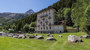 A multi-story building with balconies, surrounded by a grassy area with large rocks, and a mountainous backdrop. - Bel'Alp 16 Historical Residence Near Ski Lifts at Le Tour in Chamonix, Le Tour (Argentière), France (Le Tour (Argentière))