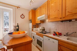 A kitchen with wooden cabinets, a built-in oven, a dishwasher, and a window with a view of snow-covered trees. - Bel'Alp 16 Historical Residence Near Ski Lifts at Le Tour in Chamonix, Le Tour (Argentière), France (Le Tour (Argentière))