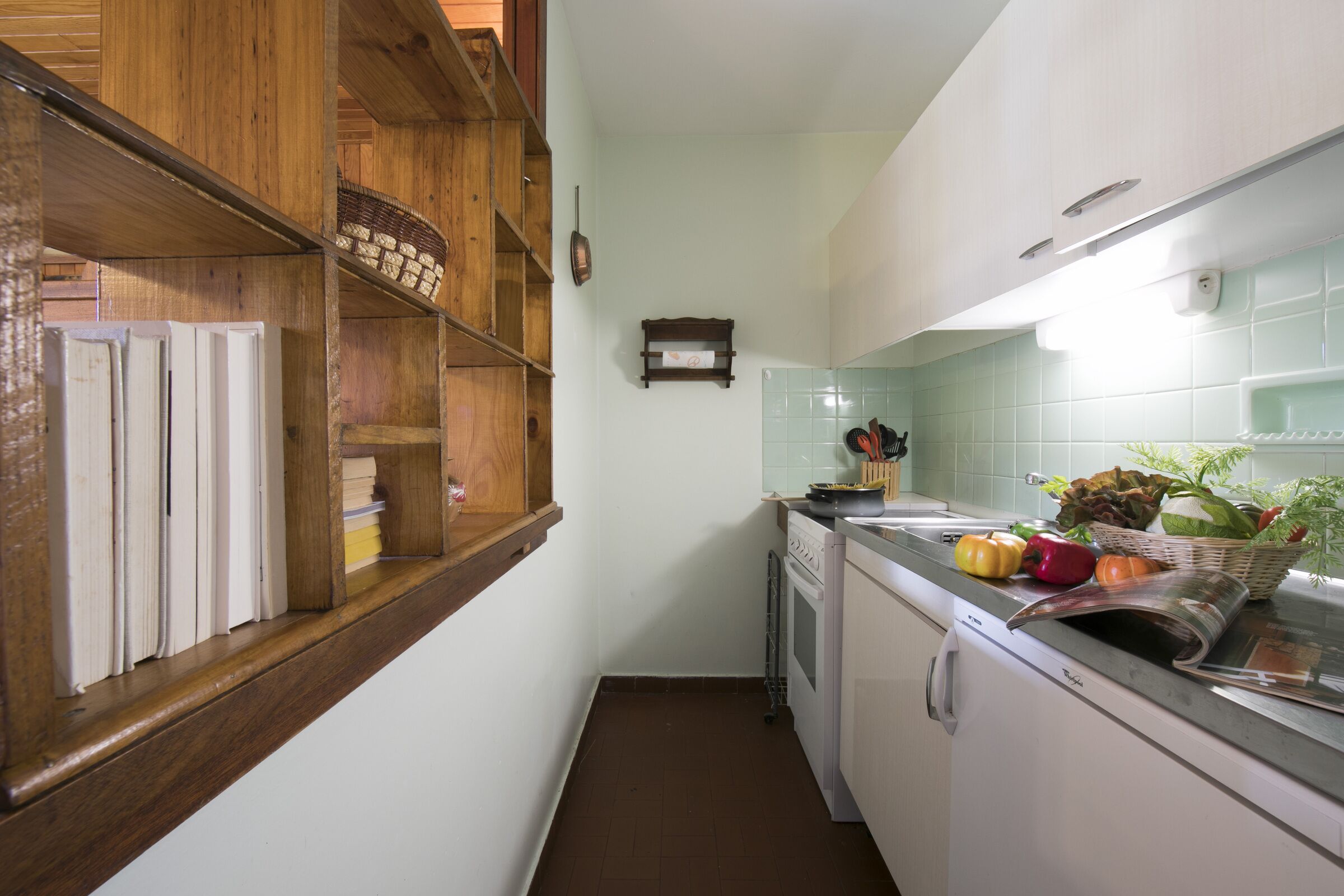 A narrow kitchen with wooden shelves, a white stove, and a tiled backsplash.
