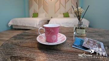 A hotel room with two beds, a wooden table with a pink cup and saucer, a bottle of perfume, and a magazine.