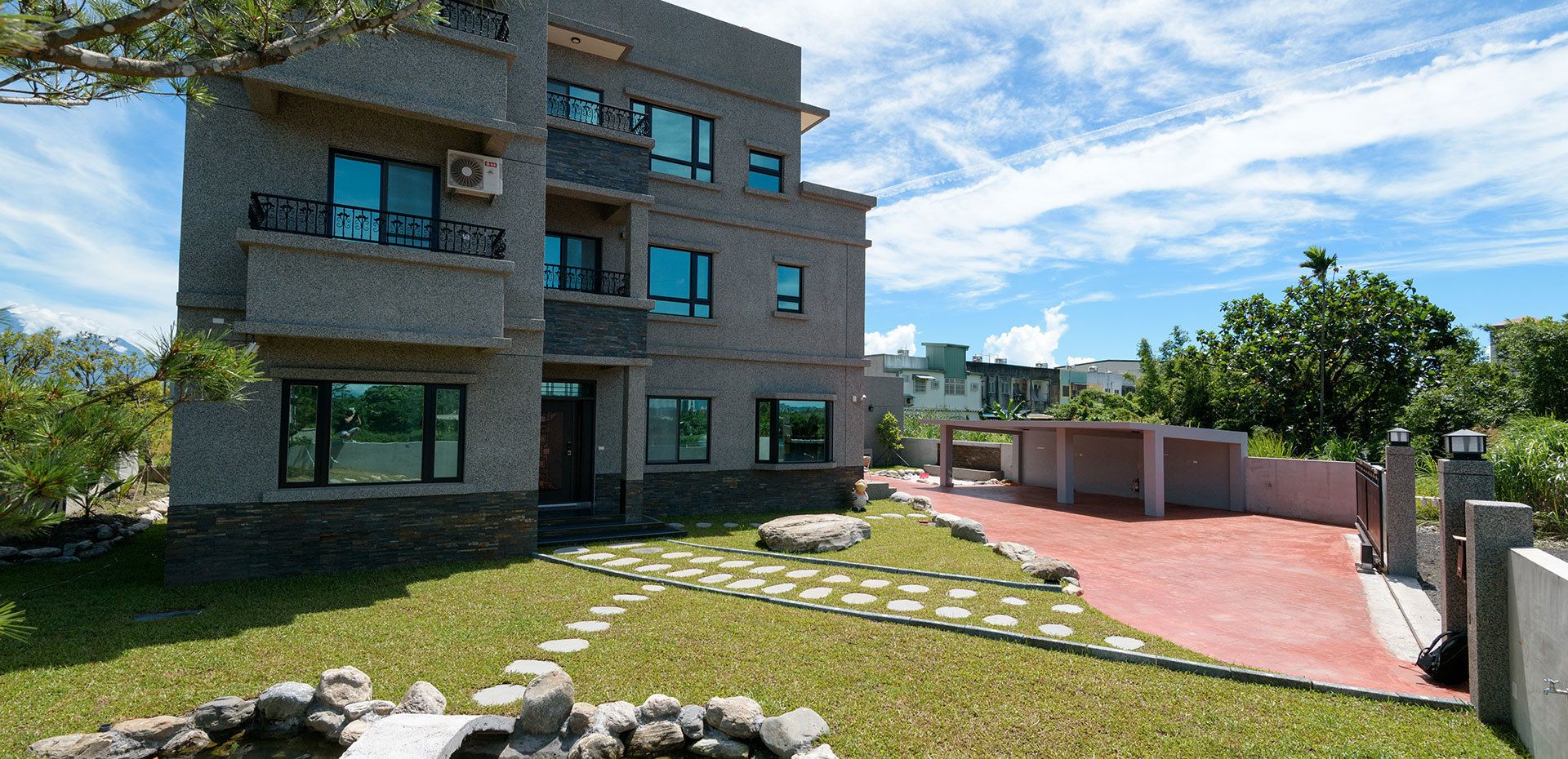 A modern multi-story building with balconies, a paved driveway, and a well-maintained lawn with stepping stones.