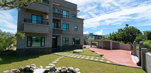 A modern multi-story building with balconies, a paved driveway, and a well-maintained lawn with stepping stones. - Melody B&B (Xincheng)