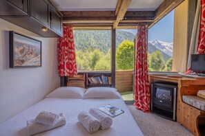 A bedroom with a bed, a bookshelf, a fireplace, and a window with curtains. - Grand Roc B9 260m from Slopes, Mountain View & Parking, Argentière (Chamonix), France (Argentière (Chamonix))