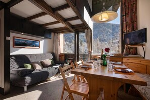 A cozy living room with a sofa, dining table, and chairs, a television, and a large window with a mountain view. - Grand Roc B9 260m from Slopes, Mountain View & Parking, Argentière (Chamonix), France (Argentière (Chamonix))