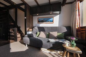 A modern living room with a grey sofa, a framed landscape painting, and a small round table with a vase and a mug. - Grand Roc B9 260m from Slopes, Mountain View & Parking, Argentière (Chamonix), France (Argentière (Chamonix))