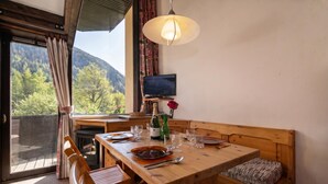 Ein Holzespeisetisch mit Stühlen, einer Bank, einem Fernseher und Blick auf einen bewaldeten Berg.
