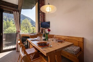 A wooden dining table with chairs, a bench, a television, and a view of a forested mountain.
