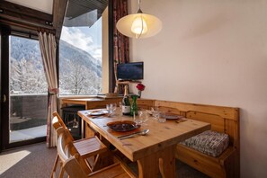A wooden dining table with chairs, a bench, a television, and a view of snow-covered mountains. - Grand Roc B9 260m from Slopes, Mountain View & Parking, Argentière (Chamonix), France (Argentière (Chamonix))