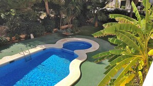 Una piscina de forma singular, rodeada de abundante vegetación y un césped cuidado.