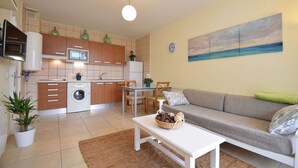Un espacio habitable compacto con kitchenette, un sofá, una mesa de comedor y una lavadora.