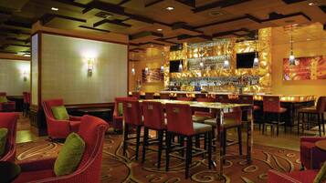 A bar area with a patterned wall, red upholstered chairs, and a bar counter with a television.