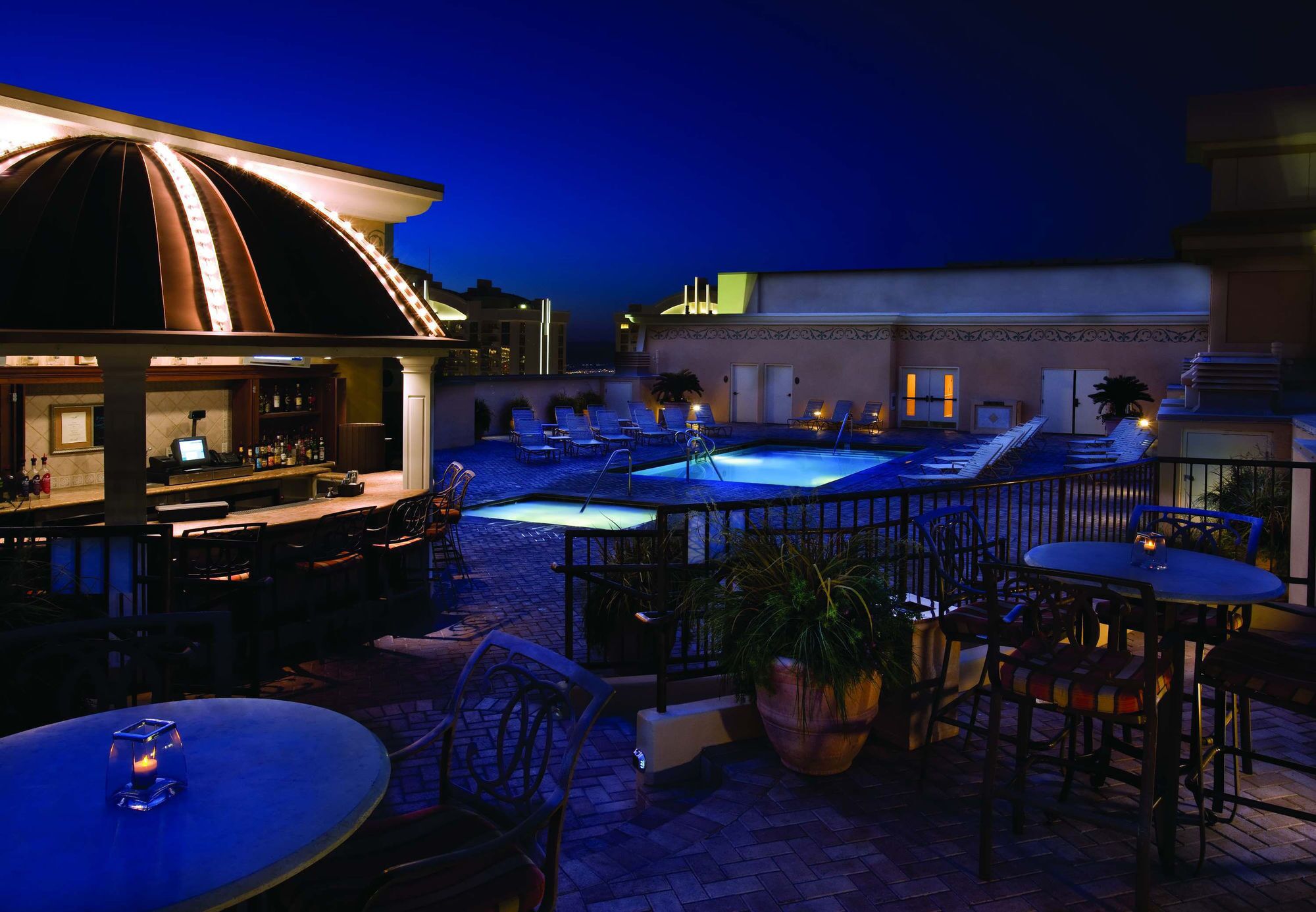 A rooftop bar with a pool, lounge chairs, and tables.