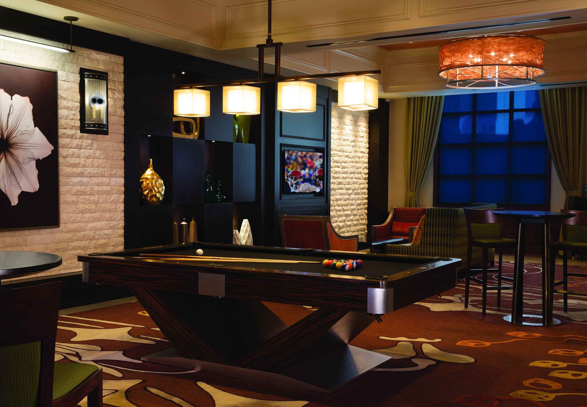 A pool table in a room with a brick wall, a large mirror, and a chandelier.