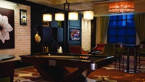 A pool table in a room with a brick wall, a large mirror, and a chandelier.